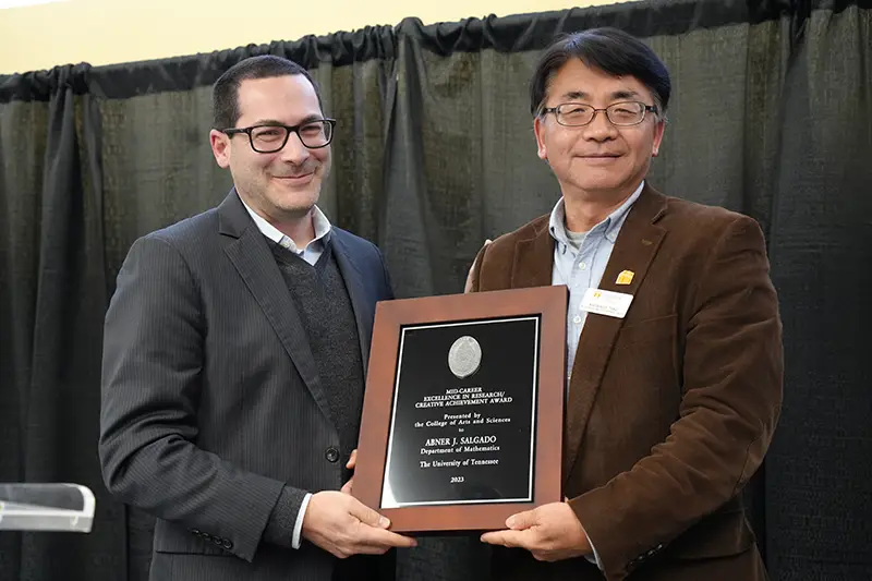 On behalf of Abner Salgado, Xiaobing Feng receives the award from Michael Blum at the 2023 Faculty Awards Convocation.