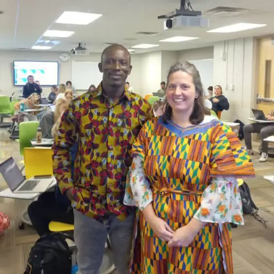 A man and a woman standing in traditional Ghana dress in a classroom on campus