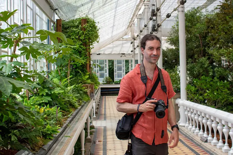 Christopher Strickland holds a camera surrounded by plants.