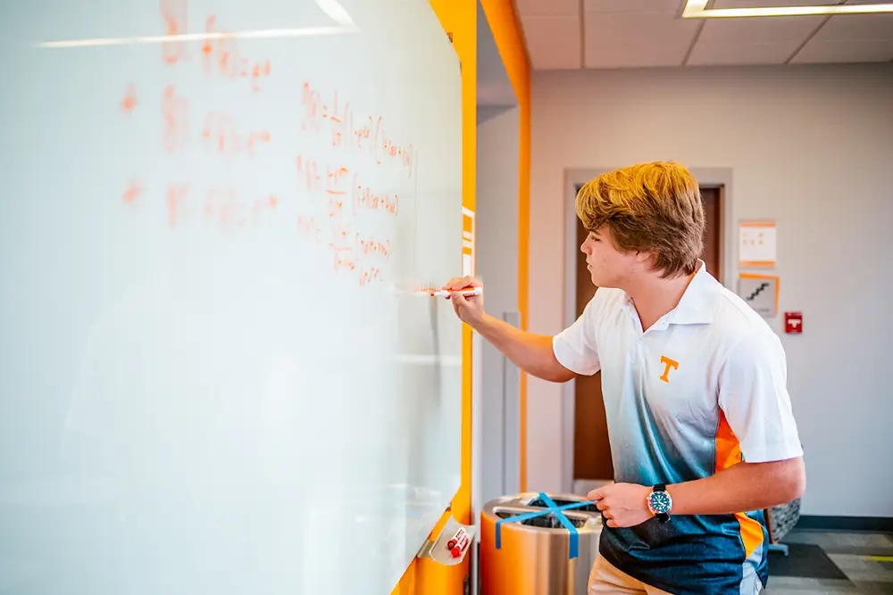 A student writes math equations on a dry erase board.