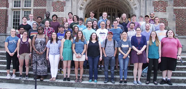 A group photo of students on the steps in front of a brick academic building